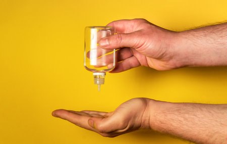 Human hands use gel, disinfectant, antiseptic in bubble, jar on yellow background. Prevention of diseases and infectionsの写真素材