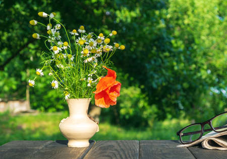 Bouquet of summer flowers and a newspaper with reading glasses on a wooden table in the garden. Summer background.の写真素材