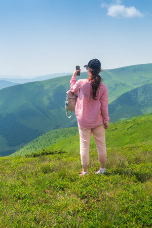 A tourist is relaxing in nature and uses the Internet on a smartphone. The girl traveler photographs a panorama of the mountains on a mobile phone. Mountain beautiful landscapeの写真素材