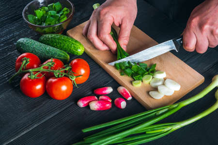 Professional chef hands close-up cuts young green onions. Cooking salad in the restaurant kitchen....