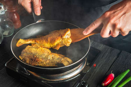 Cook or chef prepares fish in the restaurant kitchen. Boil or fry crucian carp in pan. The idea of a...