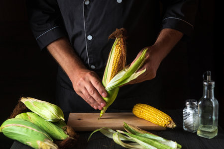 The chef peels ripe corn from the shell before cooking. Working environment in the restaurant kitchen. The hands of the cook close-up while working.の写真素材