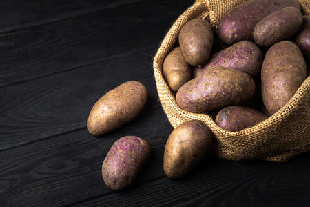 Sack of potatoes after harvest on dark vintage wooden planks. Organic potato for cooking. Free advertising spaceの写真素材