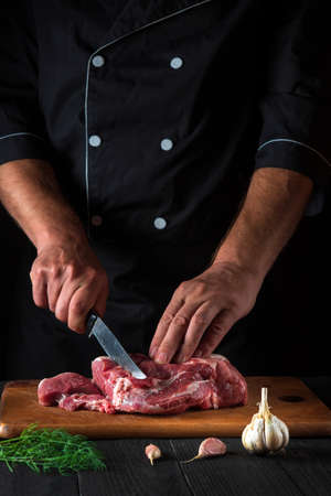 Professional chef cuts meat with a knife in the kitchen prepares food. Vegetables and spices on the kitchen table in a restaurant to prepare a delicious lunchの写真素材