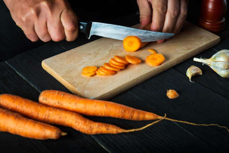 Close-up of a chef hand cutting carrots on a cutting board. Professional preparation of a carrot...