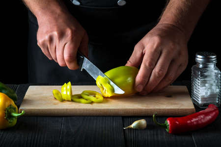 Professional chef is cutting bell peppers for salad in the restaurant kitchen. Close-up of a cook hands while working. Free advertising spaceの写真素材