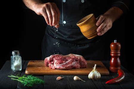 Professional chef sprinkles the meat with salt. Preparing meat before baking. Working environment in the kitchen of a restaurantの写真素材