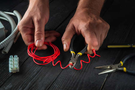 Repair of electrical equipment in the workshop of professional master electrician. Close-up of hands of electrician foreman while working or cutting red wireの写真素材