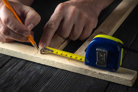 A carpenter makes pencil marks on a block of wood. Hands of the master close-up at work. Working environment in a carpentry workshopの写真素材