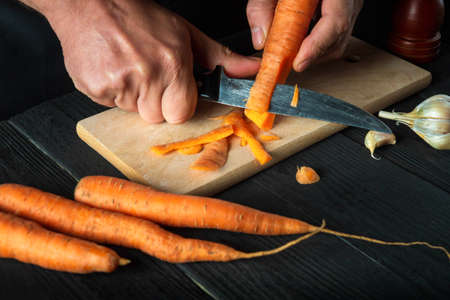 A professional chef peels carrots for vegetable soup in a restaurant kitchen. Close-up - hands of the cook during work. Carrot dietの写真素材