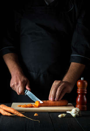 Professional chef is cutting carrots for vegetable soup in the restaurant kitchen. Close-up of the hands of the cook during work. Carrot dietの写真素材