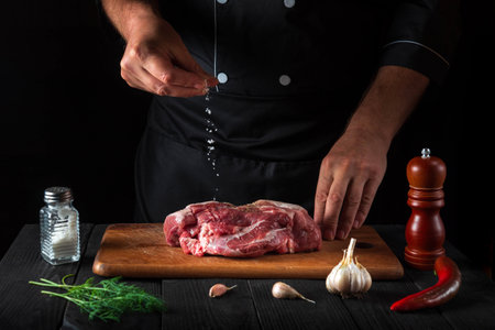 Cook sprinkles the meat with salt. Preparing meat before baking. Working environment in the kitchen of a restaurantの写真素材