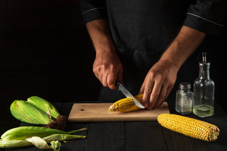 The chef cuts fresh corn with a knife. Boiled corn is a great diet for breakfast or lunch. Working environment on the restaurant kitchen tableの写真素材