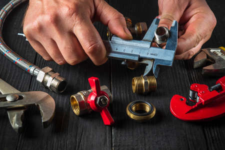Professional wizard measures the size of fitting using a caliper before connecting water or gas pipe. Close-up of the hands of the master plumberの写真素材