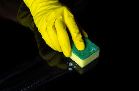 Hand cleaning black desk with a yellow washcloth. Close up shot of a home cleaning process. Health care during coronavirus and disinfection concept.の写真素材