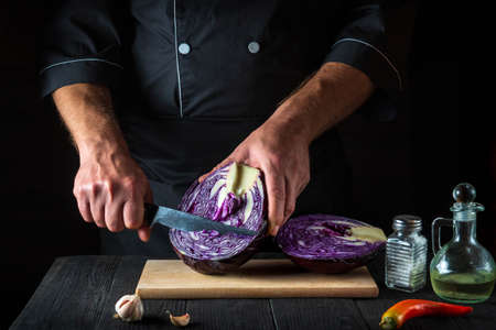 The cook is cutting red cabbage with a knife. Cooking vegetable salad in the restaurant kitchen. Vegetable diet ideaの写真素材