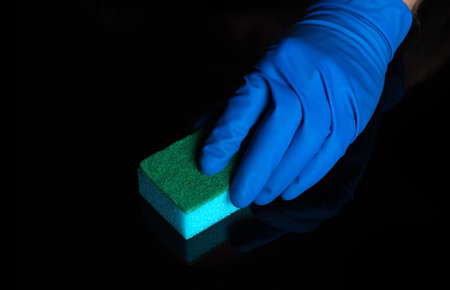 Hand cleaning black desk with a blue washcloth. Close up shot of a home cleaning process. Health care during coronavirus and disinfection conceptの写真素材