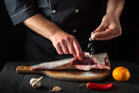 Professional chef prepares fresh fish sprinkling salt. Preparing to cook fish food. Working...