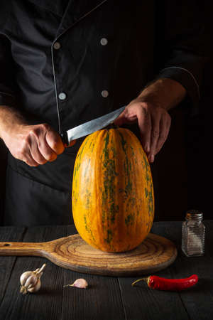 Professional chef cuts a ripe yellow pumpkin with a knife before baking. Baked pumpkin is a great diet for breakfast or lunch. Working environment on the kitchen table of the restaurant.の写真素材
