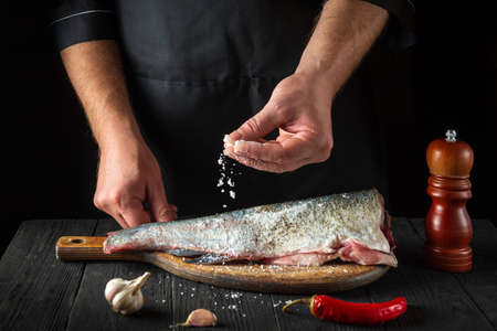 The chef prepares fresh fish sprinkling salt. Preparing to cook fish food. Working environment in the restaurant kitchen.の写真素材