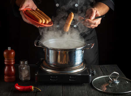Chef cooks Vienna sausage in a saucepan. Working environment in the restaurant kitchen. Delicious breakfast or dinnerの写真素材