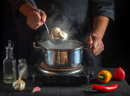Cook cooks meat dumplings in a saucepan in the restaurant kitchen. Close-up of the hands of the cook during work. Free advertising space.の写真素材