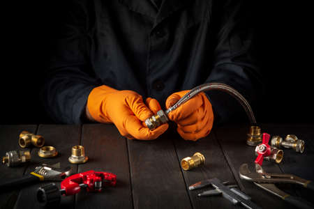 Professional plumber connects brass fittings to plumbing hose. Close-up of hand of the master during work in workshopの写真素材