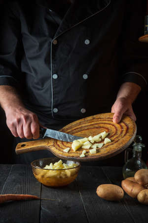 The chef prepares raw potatoes for lunch or dinner. Close-up of a cook hands while working in a restaurant kitchen.の写真素材