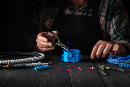 Close-up of hands of a master electrician during work. Installing a cable or wire to blue junction...