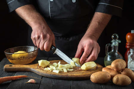 Before preparing the national dish, the chef cuts raw potatoes into small pieces with a knife. Close-up of a cook hands while working in a restaurant kitchen.の写真素材