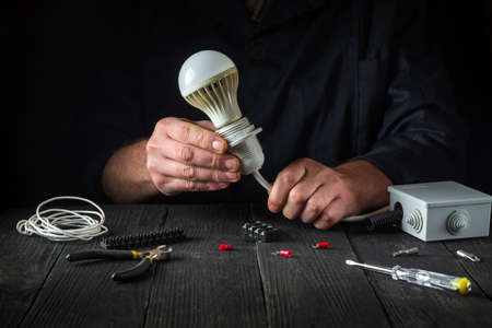 The master electrician connects the light bulb. Close-up of working hands at work table in workshop...
