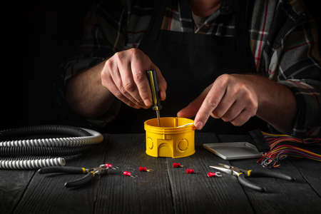 Close-up of hands of a master electrician during work. Installing a cable or wire to yellow junction...