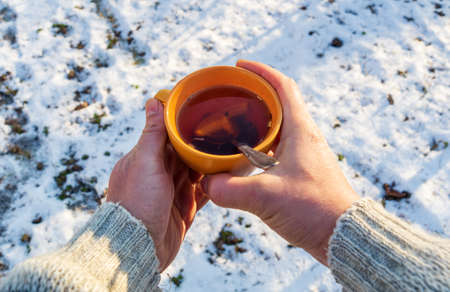Person hands hold an orange mug of hot herbal tea in cold winter. Prevention of viral diseases lemon teaの写真素材