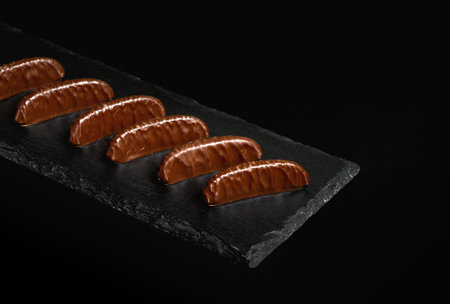 Sweets or candies on a black serving board. Assorted chocolate on a black isolated background. Free...