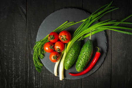 Fresh vegetable salad set. Red tomatoes and green young onions with cucumber on a black plate. Vitamin breakfast or dinner.の写真素材