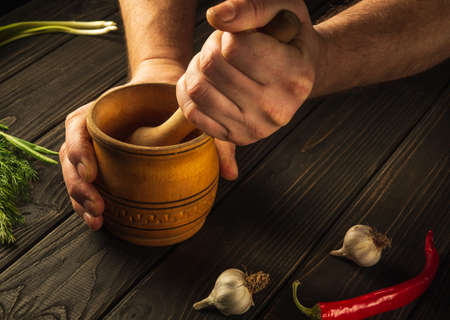Cook crushing a blending garlic in a wooden pestle and mortar in a close up view on his hands. Cooking a national dish in the kitchenの写真素材