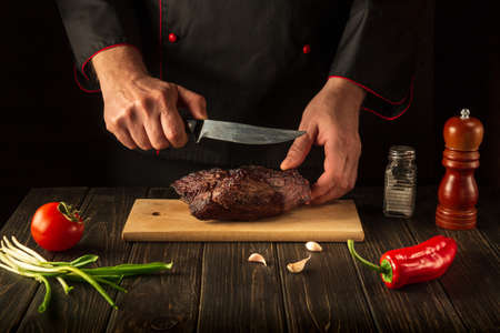 Preparing for cutting baked beef meat on a cutting board. The idea of preparing a delicious lunch by a chef. Copy space for text menu or recipeの写真素材