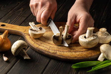 The cook cuts Agaricus mushrooms on a cutting board. Close-up of a chef's hands with a knife. Vegetarian food.の写真素材