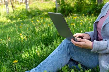 Rest with a laptop in nature in the park on a sunny day against the backdrop of green grass. Woman freelancing outdoors.の写真素材