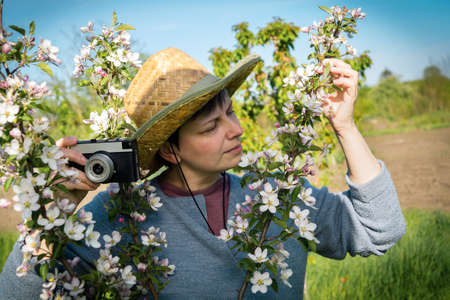 Photography as an interesting hobby. Middle-aged woman in a straw hat holding a vintage camera among...