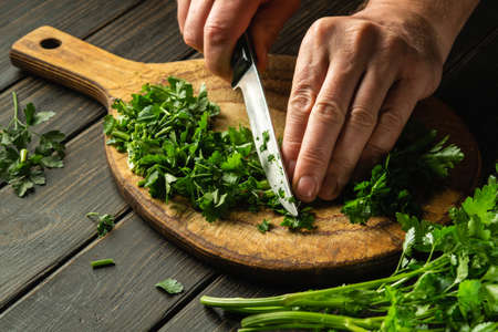Cutting green parsley on a cutting board with a knife for cooking vegetarian food. Peasant food.の写真素材