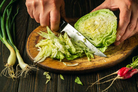 Slicing cabbage on a cutting board. Delicious salad for dinner with fresh vegetables. Hands of a...
