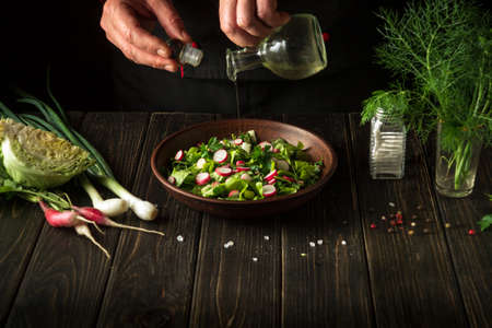 The chef adds vegetable oil to a plate with a delicious salad. Diet breakfast with fresh vegetables.の写真素材