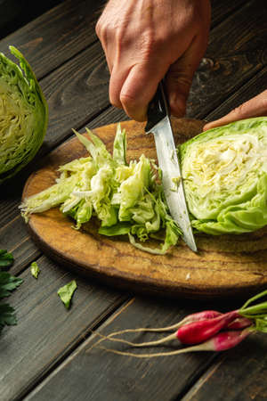 The chef cuts fresh cabbage with a knife on a cutting board before preparing a vegetarian dish.