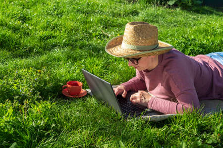 Freelancing outdoors in the garden. A woman with a laptop works on the lawn. The idea of effective...