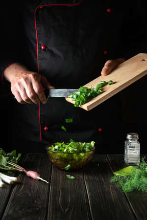 Adding chopped green onions to a fresh vegetable salad. Chef while cooking delicious food in the...