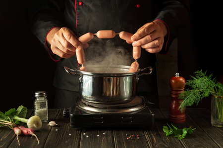 The chef puts the Viennese sausages into the pan. Working environment in the kitchen of a restaurant...