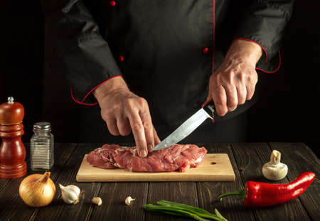 Experienced chef cuts raw beef meat on a cutting board before baking. Hotel menu recipe ideas