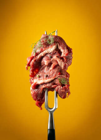 Raw beef meat with spices and dill on a fork before grilling or barbecue. Menu concept for hotel on yellow backgroundの写真素材