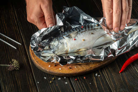 The chef prepares mackerel on the kitchen table. The fish is wrapped in foil before baking to preserve the aroma and taste.の写真素材